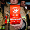 Firefighter holding a bag of Fire Department Coffee Original Medium Roast Coffee 12 ounce bag.